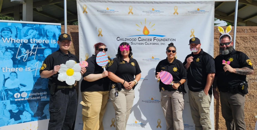 6 DAPO staff stand in front of sign for Childhood Cancer Foundation with Easter themed props