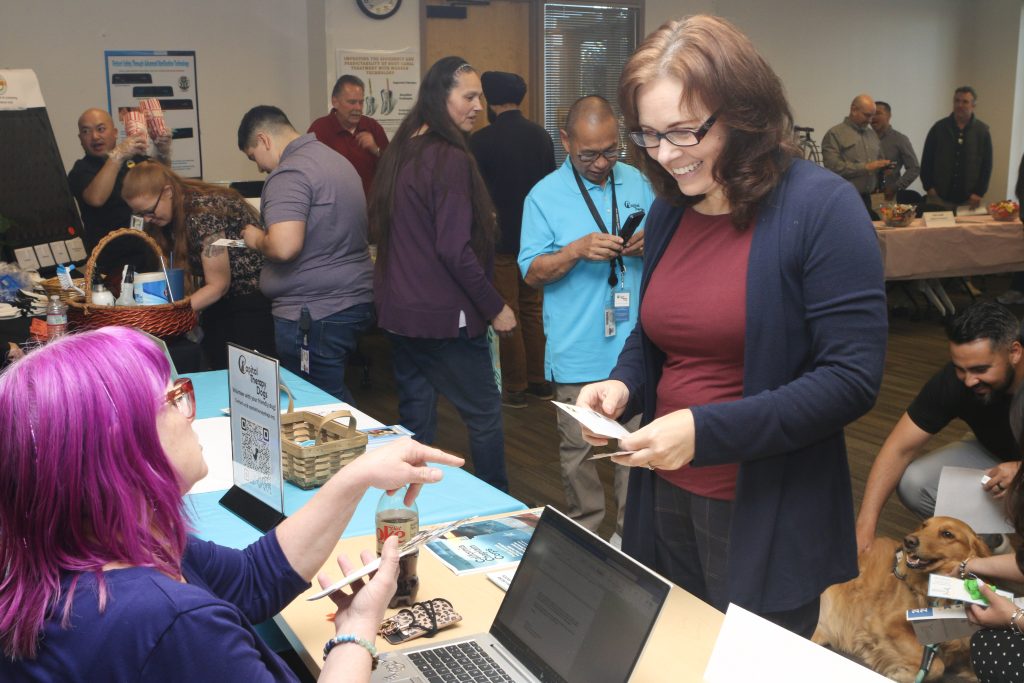 multiple staff at patient safety fair, woman holding educational materials interacts with another woman at the capital therapy dogs booth