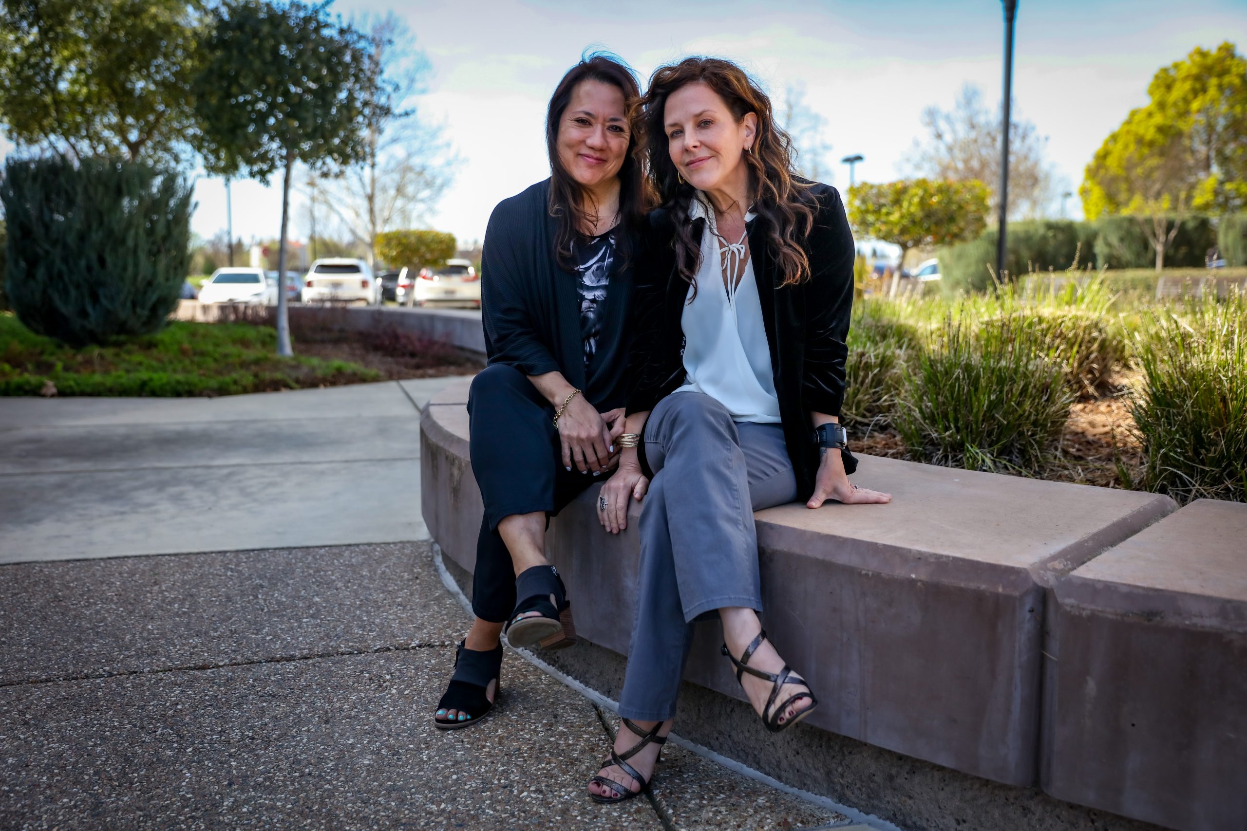 Two women sit next to each other outside on concrete bench