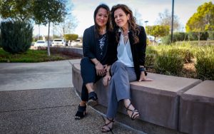 Two women sit next to each other outside on concrete bench