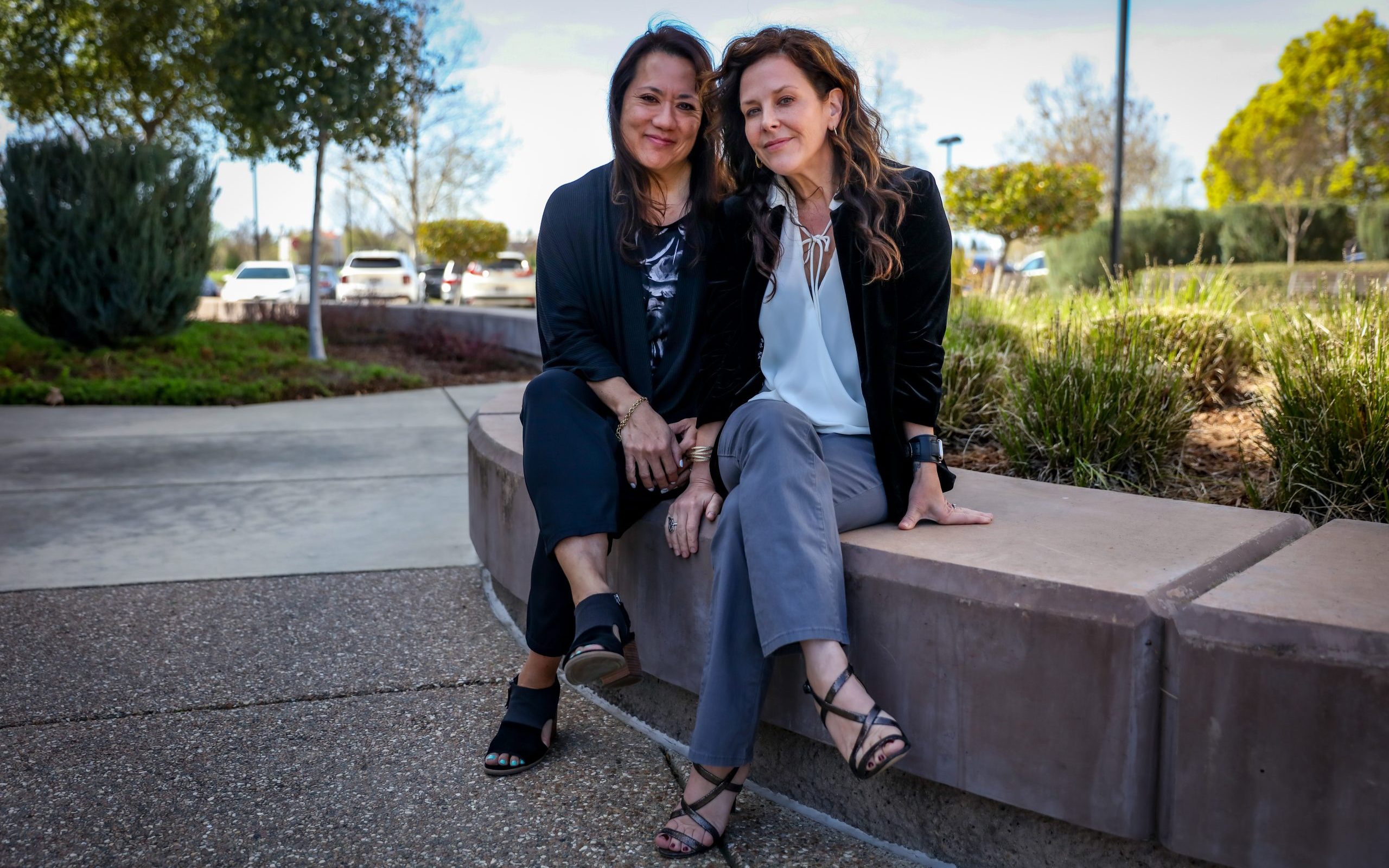 Two women sit next to each other outside on concrete bench