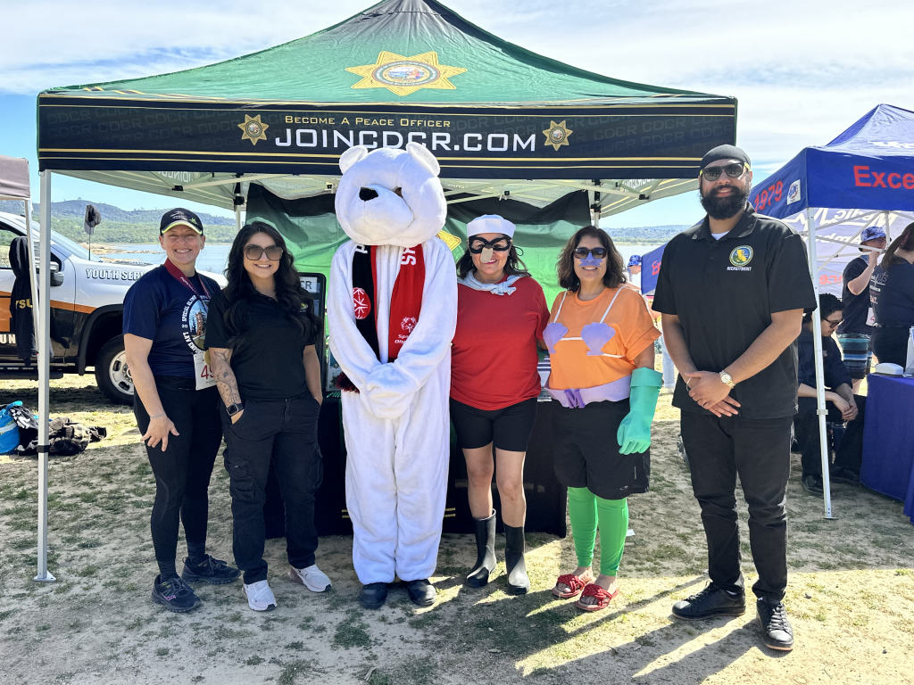 5 CDCR Recruitment staff stand in costume with polar bear mascot at Granite Bay Main Beach for Special Olympics Polar Plunge