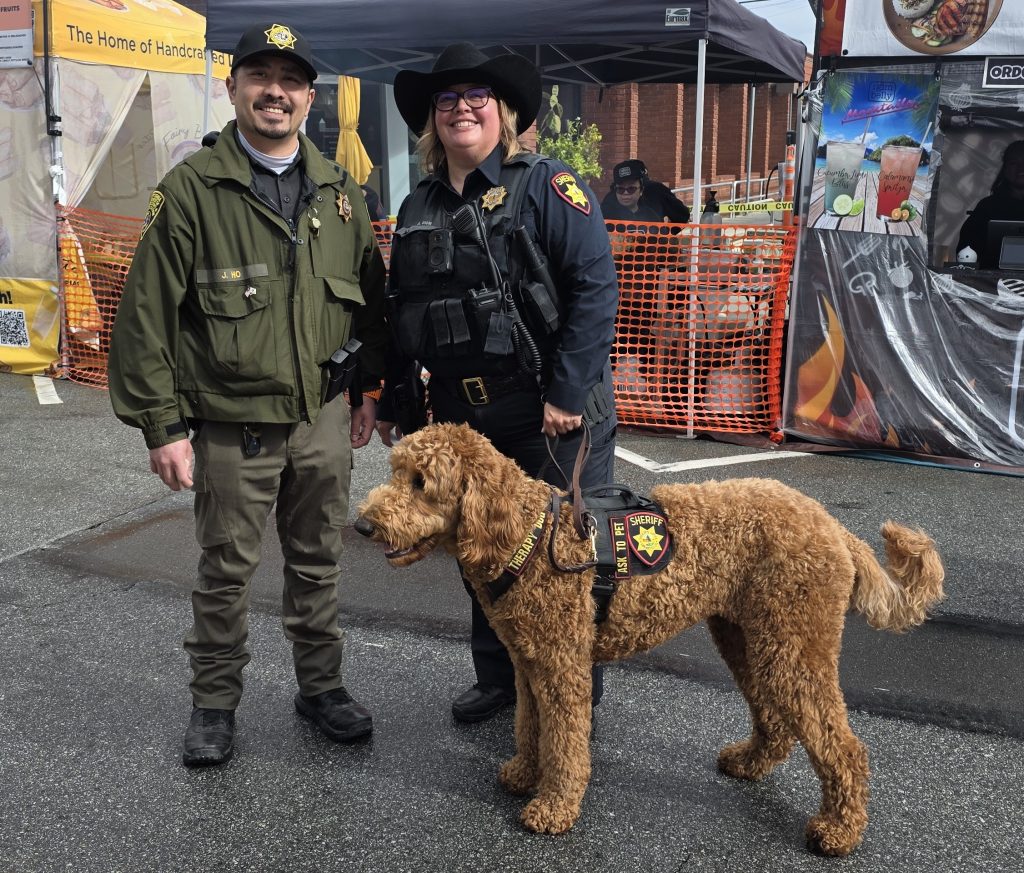 SQRC recruiter at Lunar New Year celebration with a sheriff's deputy and a therapy dog.