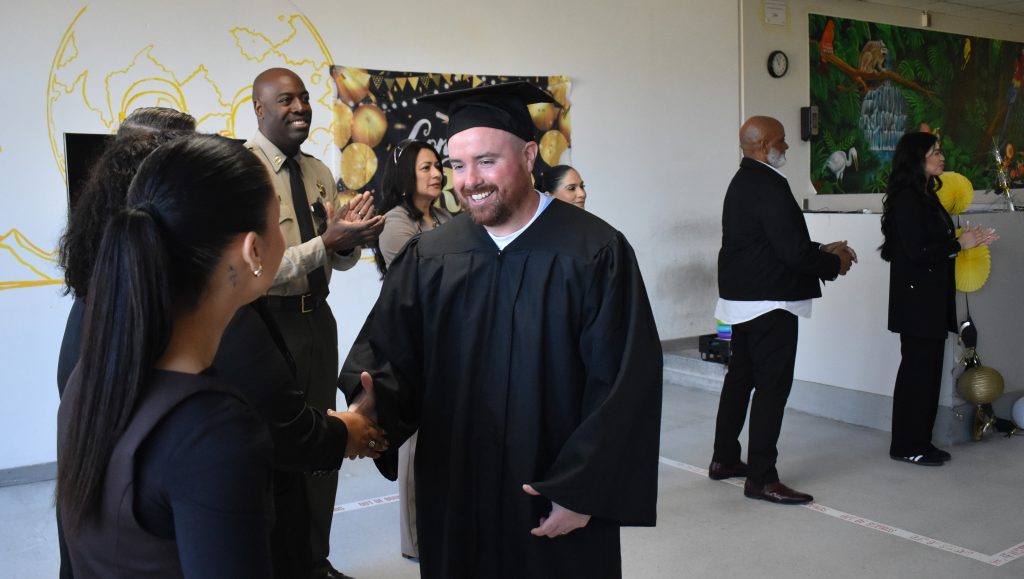 ISUDT graduate shakes hands with staff member, other staff member stand in background