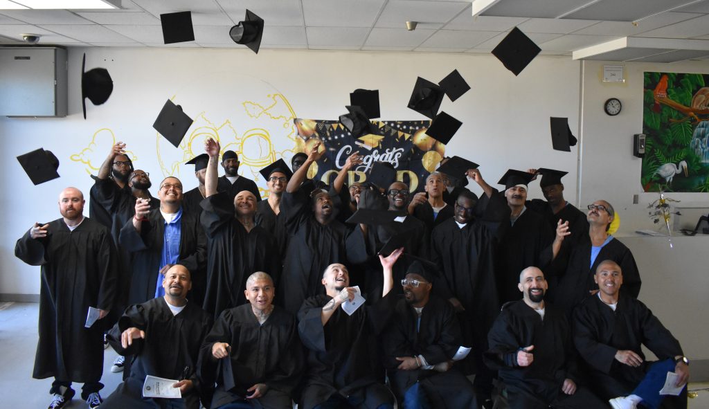 Large group of incarcerated graduates throw their graduation caps in the air