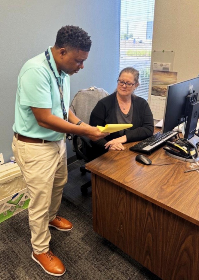 Two staff looking at paper, one standing up one sitting at desk