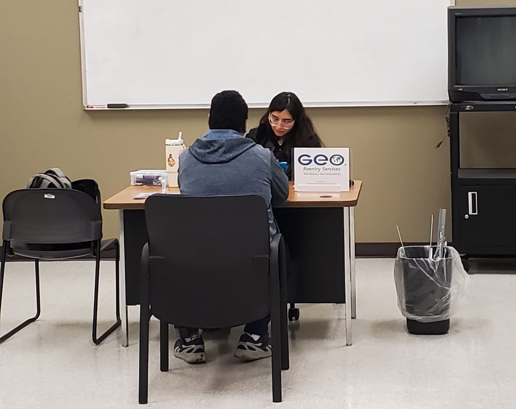 Female staff member meets with an individual at her desk with reentry services sign on desk