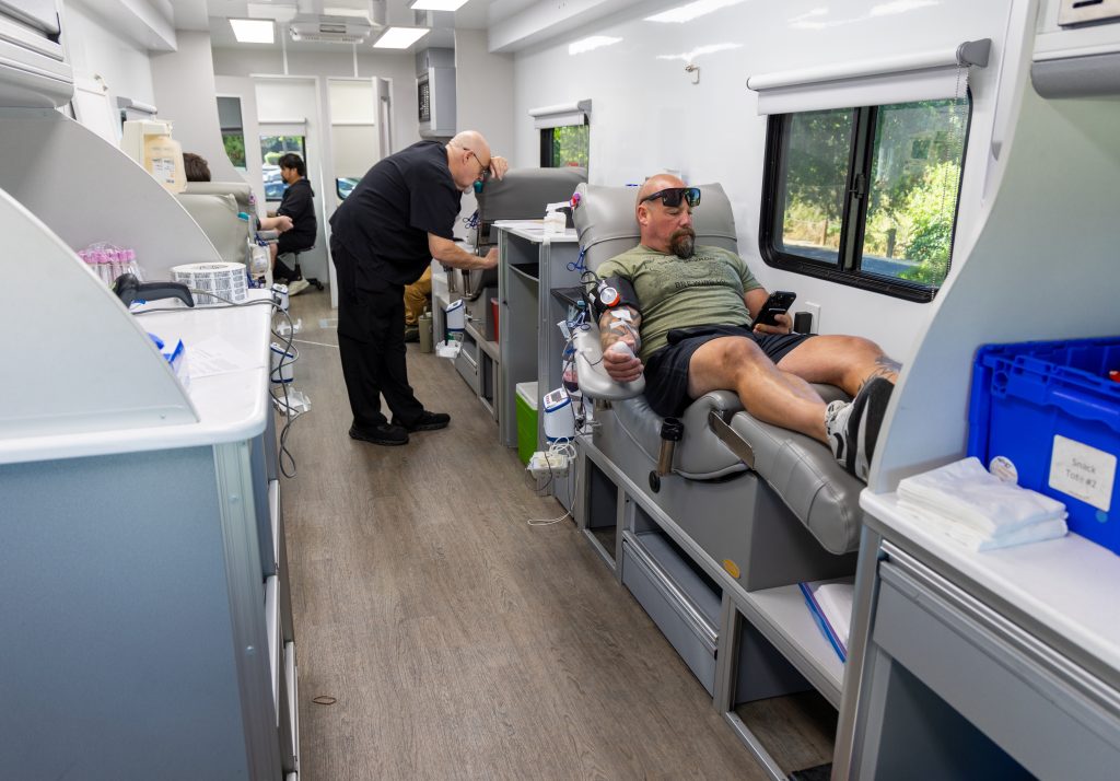Staff member sits in chair to get his blood drawn, two Vitalant staff working