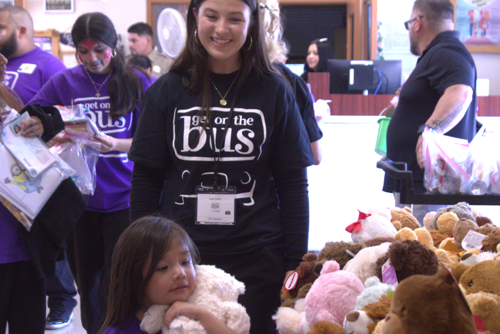 child with teddy bear and people with "get on the bus" t-shirts