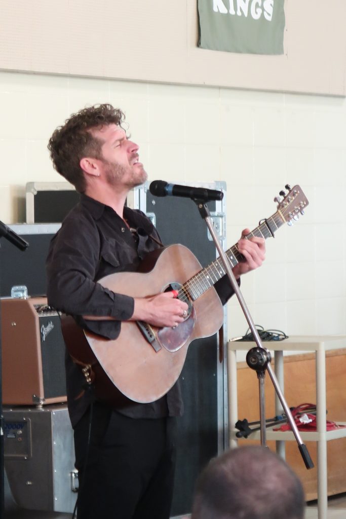 Man holds guitar and sings into microphone