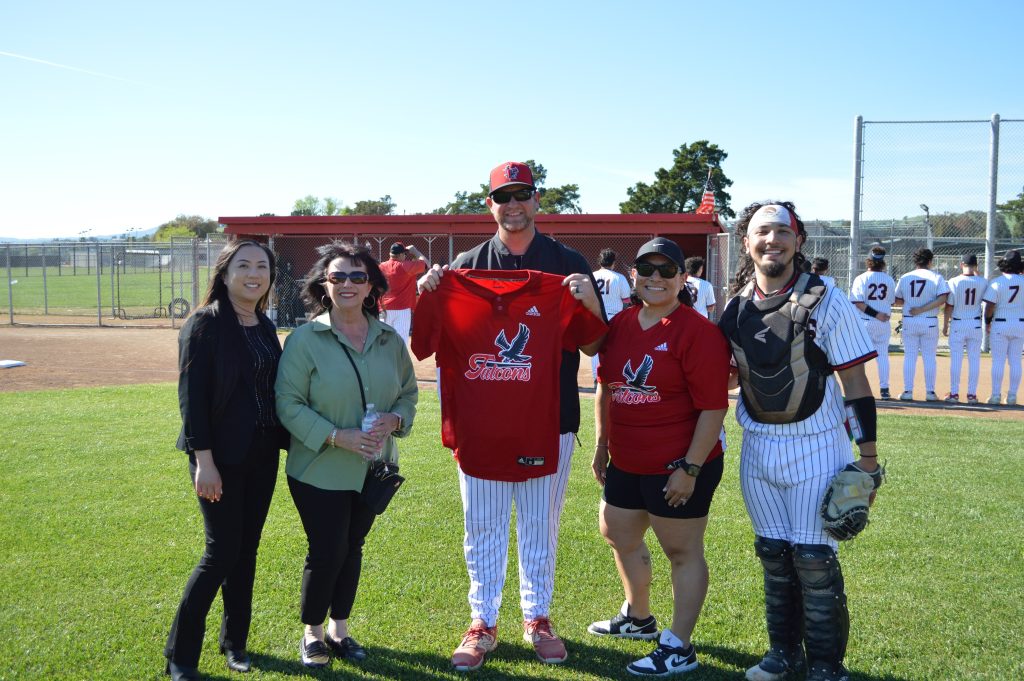 CSP SOL staff member Veronica Mitchell stands with son and basbeall team member on Fairfield Falcons baseball field, and 3 additional unidentified participants, one holding up Falcons jersey
