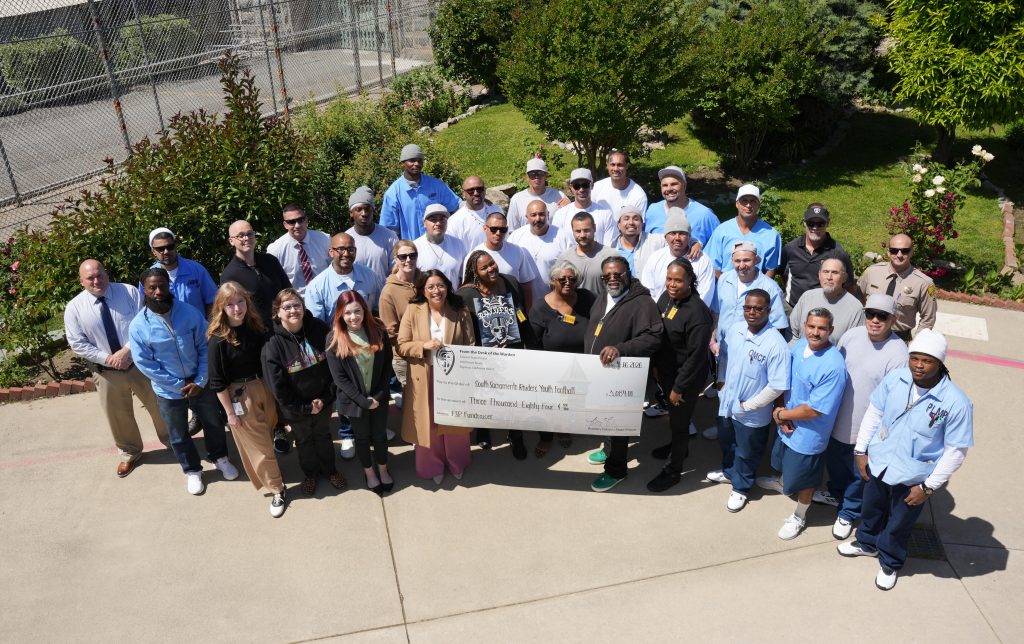 FSP staff and incarcerated pose for group photo with large check made out to youth football organization