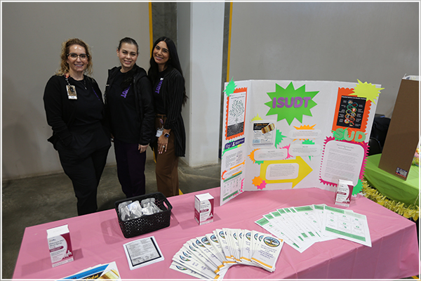 Three staff members stand behind ISUDT table booth