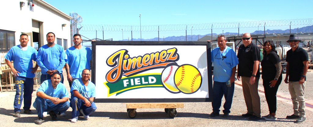 ISP staff and incarcerated persons stand with large "Jimenez Field" sign
