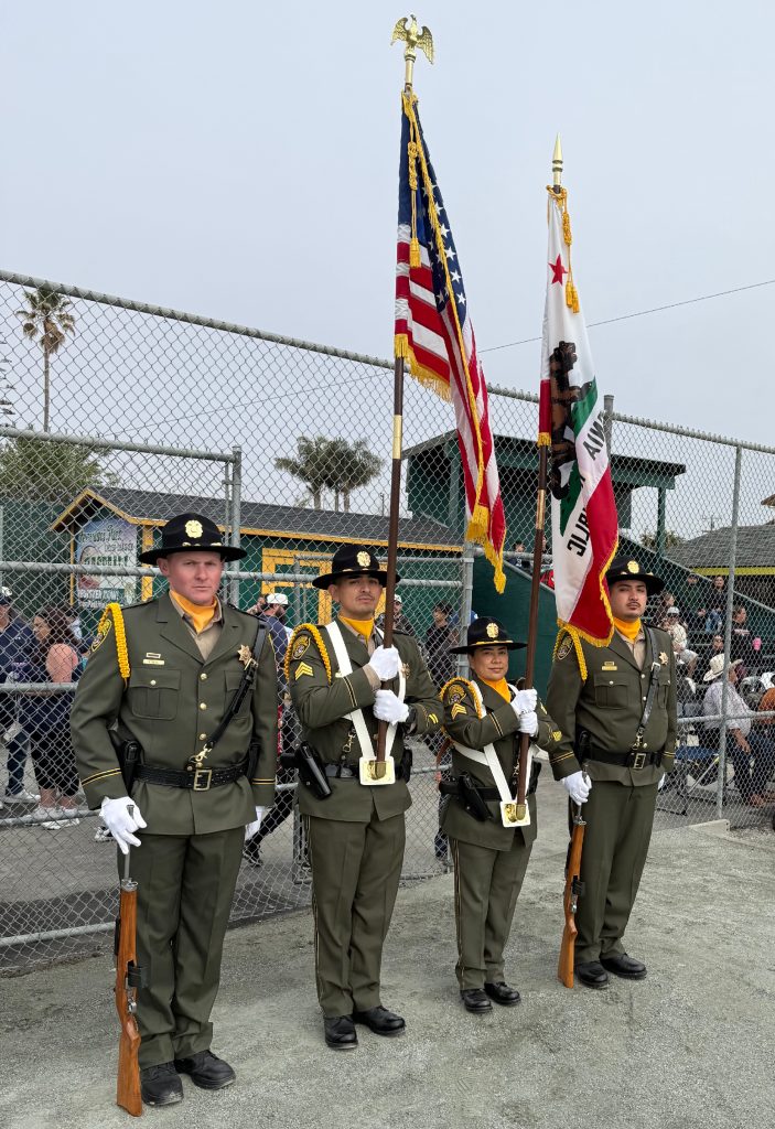 4 members of the CTF honor guard stand with American and CA flags on baseball field