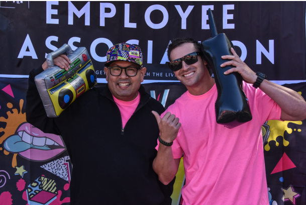 Two MCSP employees dressed in bright pink shirts and 80's themed blow up props