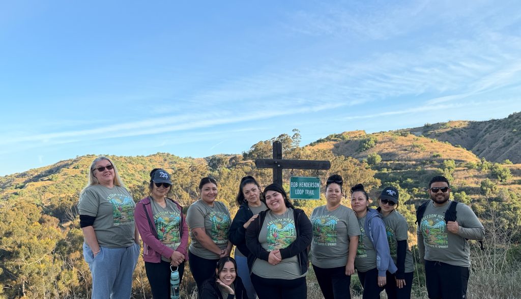 Group of Santa Fe Springs Freedom Hikers with Bob Henderson Loop Trail sign and hills in background