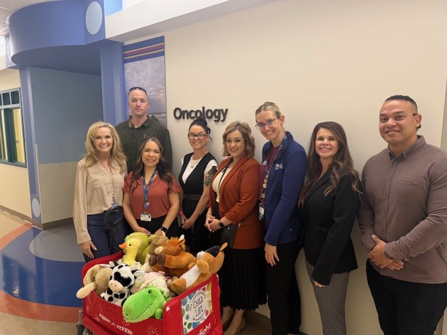 SATF staff stand with wagon full of stuffed animals at children's hospital, Oncology sign on wall behind them.