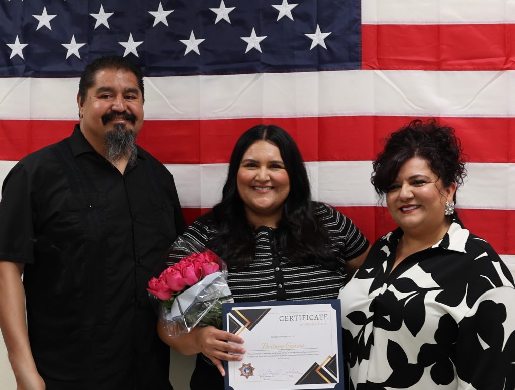 SATF staff member poses with family in front of American flag at promotion ceremony