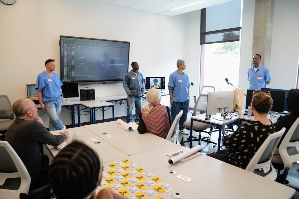 Incarcerated and staff stand in front of large digital display inside SQRC new media center