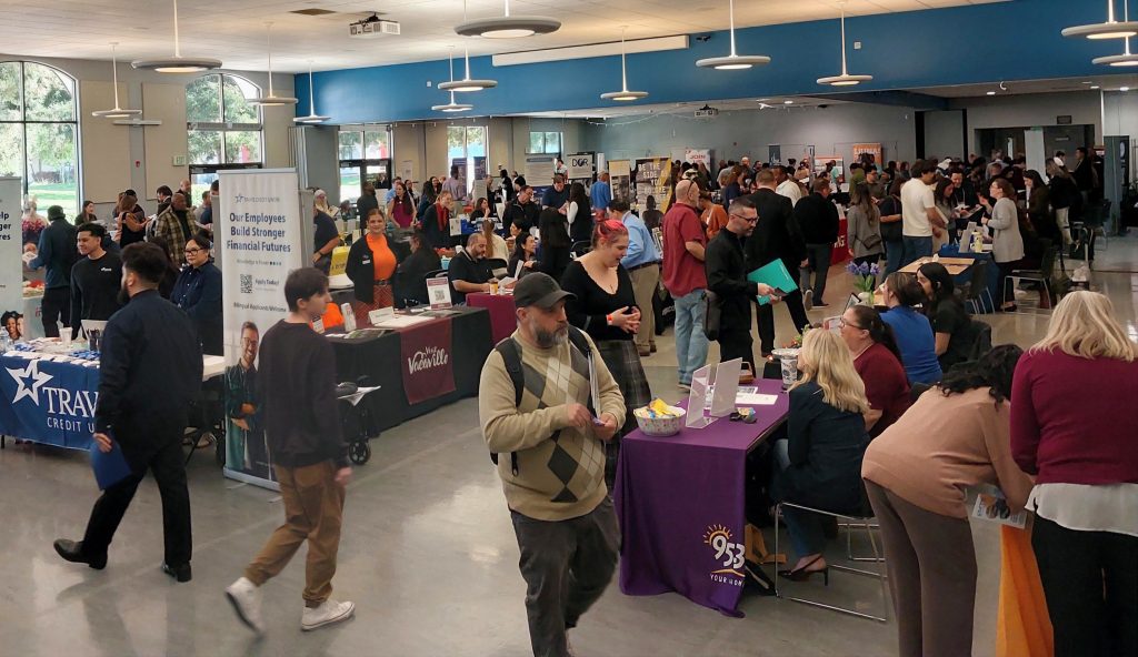 Large auditorium of people attending hiring fair and tables set up with resources