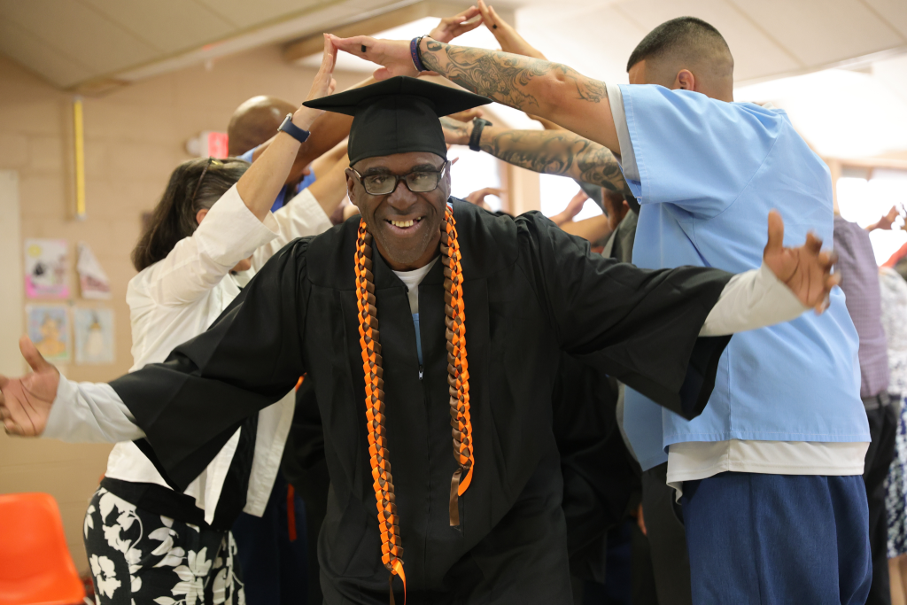 Smiling man with graduation attire walks under walkway of people's arms