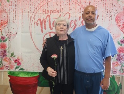 A woman holds a flower while standing beside an incarcerated man at Avenal State Prison during Mother's Day visiting.