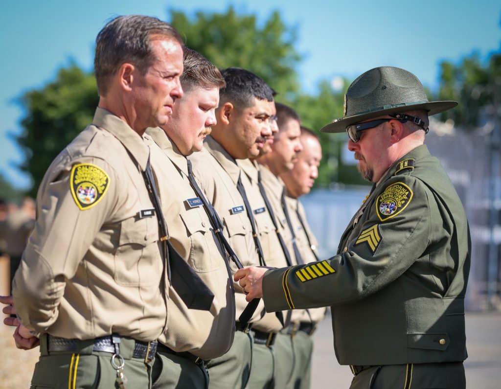 A sergeant helps a cadet adjust his tie.