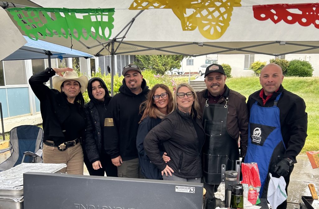 Cinco de Mayo event at CCI-Tehachapi with staff members standing under a canopy during the rain.