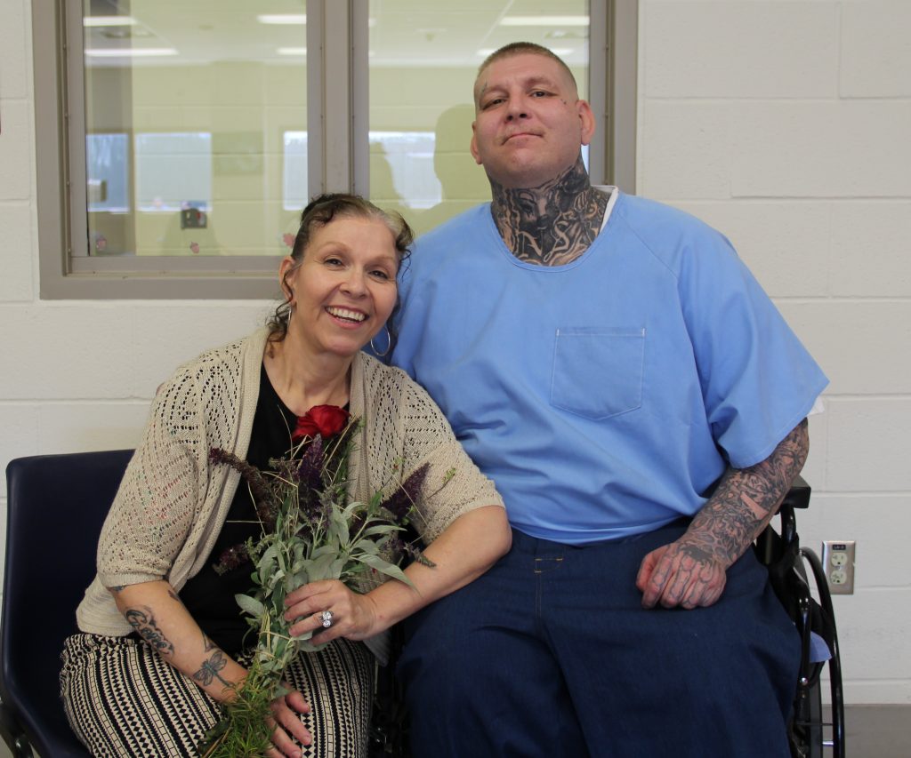 Holding flowers, a visitor sits beside an incarcerated person during Mother's Day at CHCF.