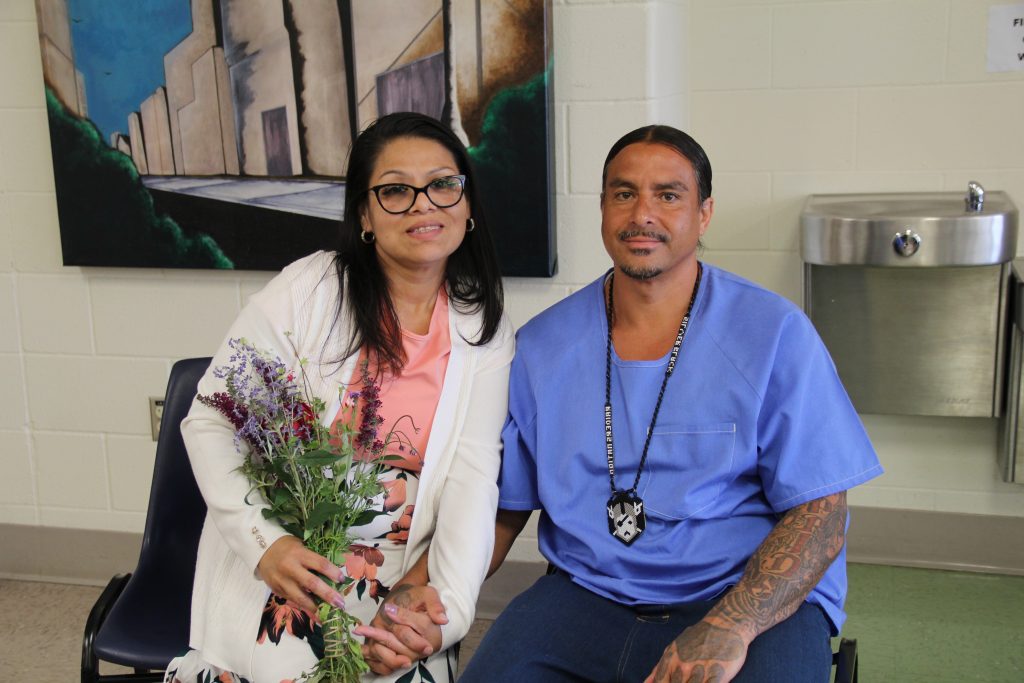 Holding flowers, a visitor sits beside an incarcerated person during Mother's Day at CHCF.