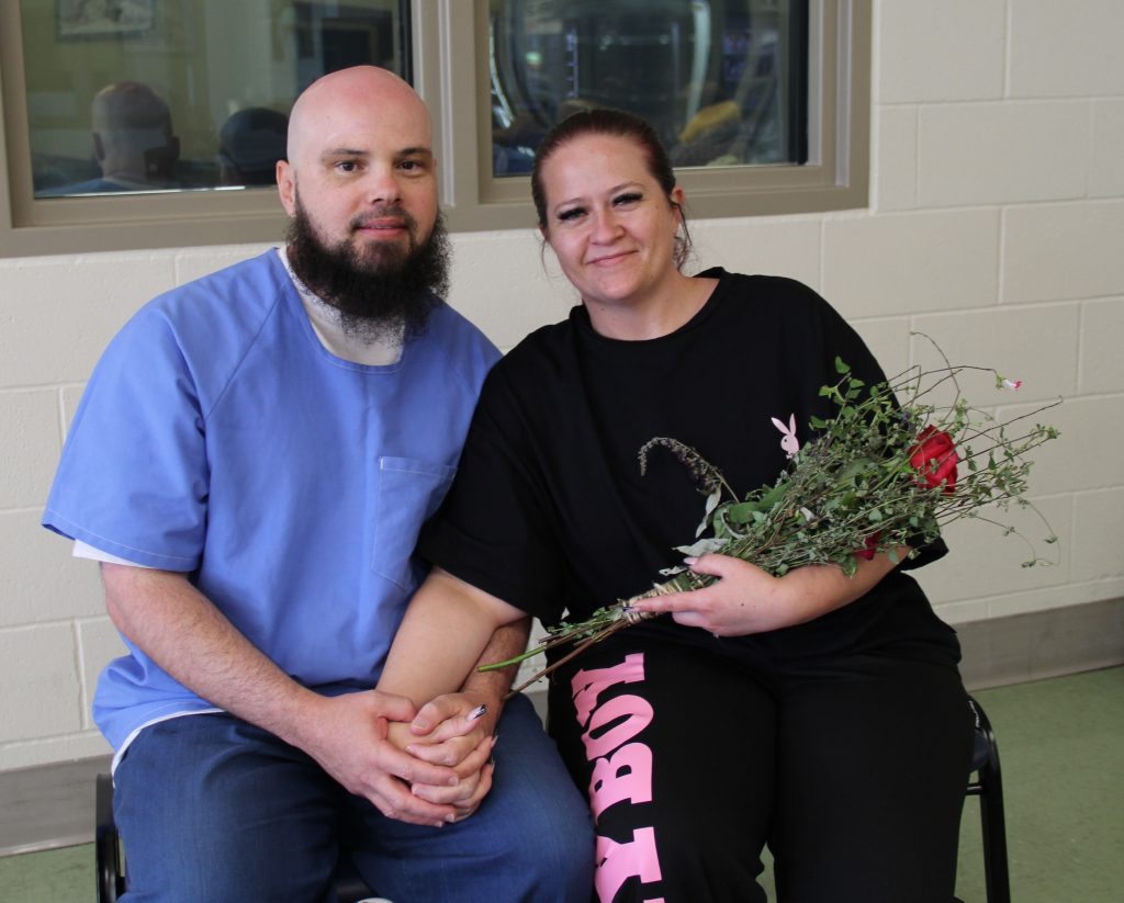 Holding flowers, a female visitor sits beside an incarcerated person during Mother's Day at CHCF.