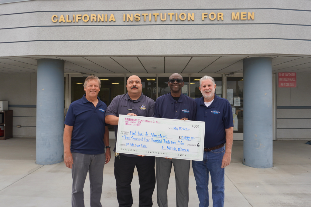 CIM Warden Eric Mejia presents a large check to Food for Life Ministries