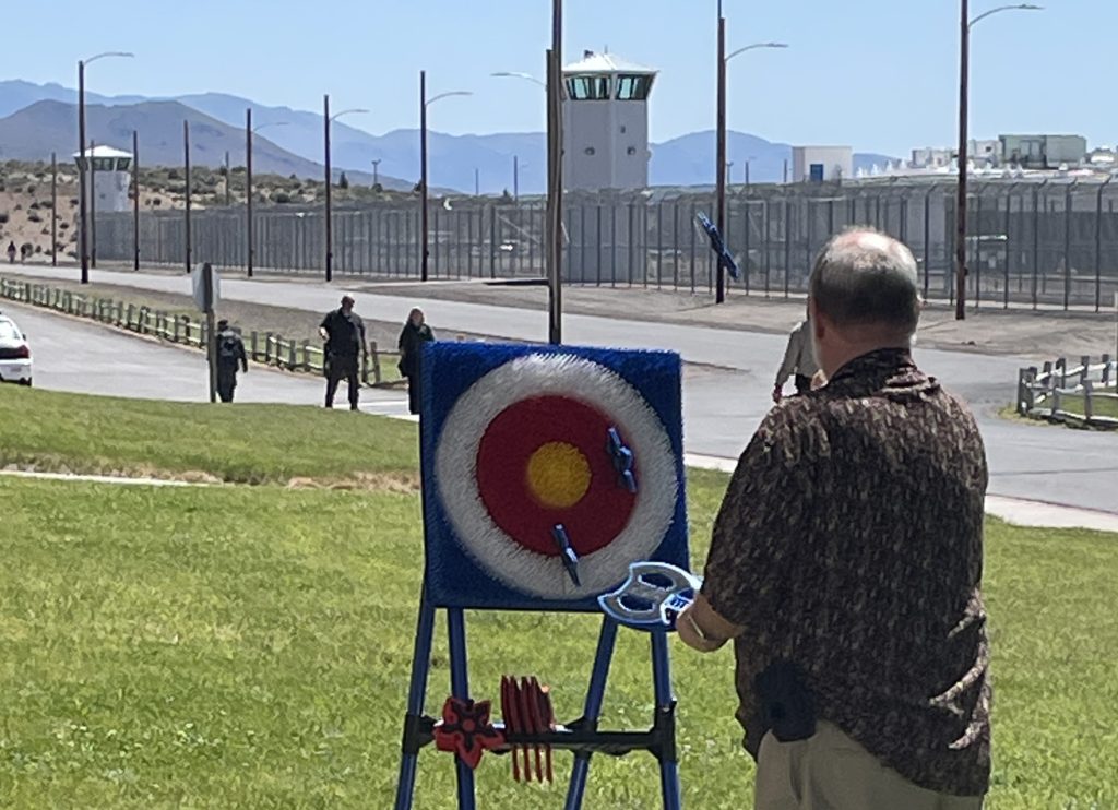 A staff member plays a plastic-ax throwing game during a staff appreciation event at High Desert State Prison in Susanville, California. In the background is fencing and a prison tower.