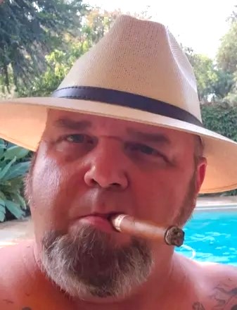 Curtis Hevener, retired correctional officer, passed away May 6, 2026. Obituary image shows man with cigar and a wide-brimmed hat.