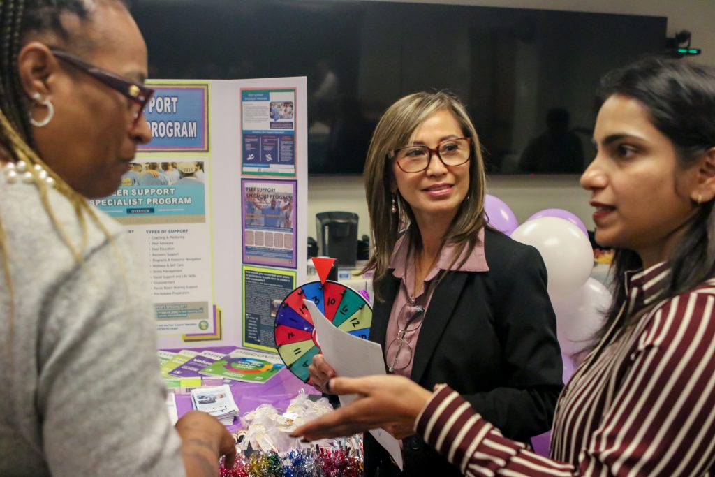 Group of staff stand at booth with interactive spinning wheel game and resources in background