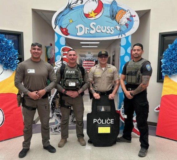 Group photo of LAC staff and a police officer standing under a Dr. Seuss banner for Read Across America Week.