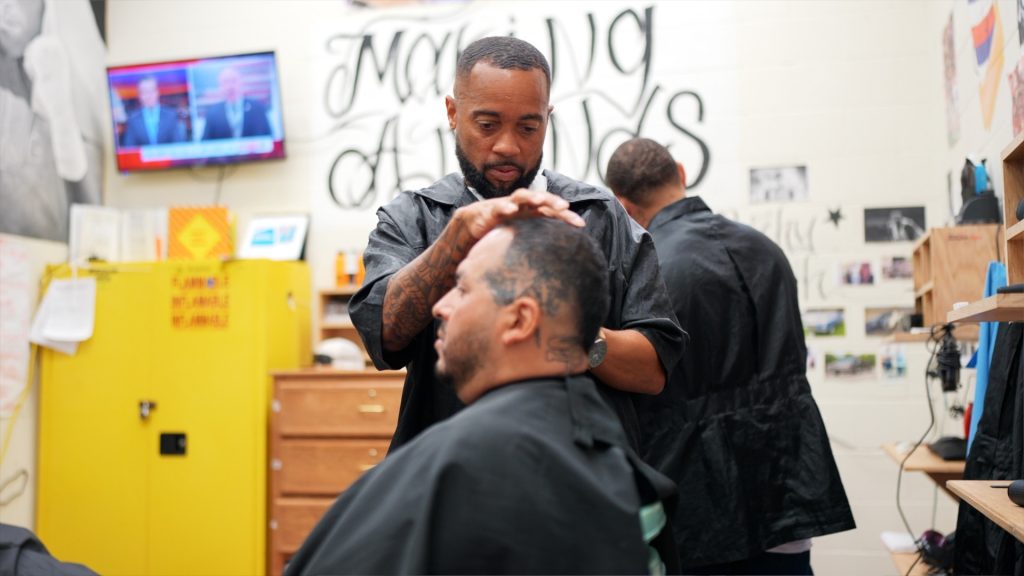 Man sitting in a barber chair getting a haircut at SATF in Corcoran, California.