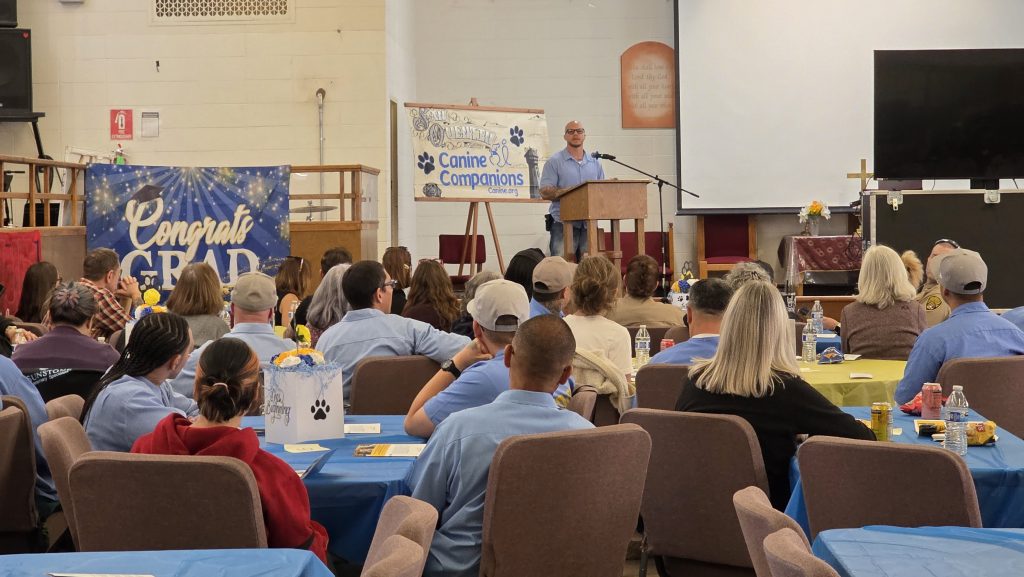 Canine Companions puppy graduation at San Quentin with a large group of people gathering a room.