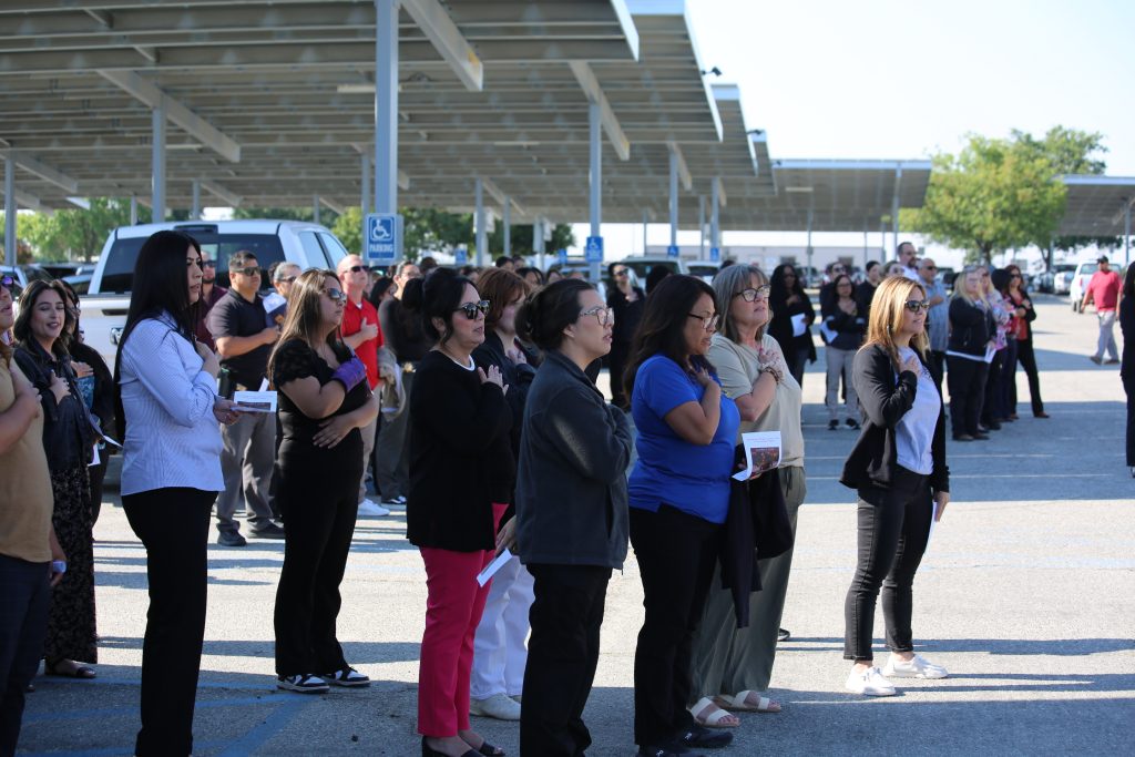 Large group of WSP staff stand in parking lot holding one hand over their heart