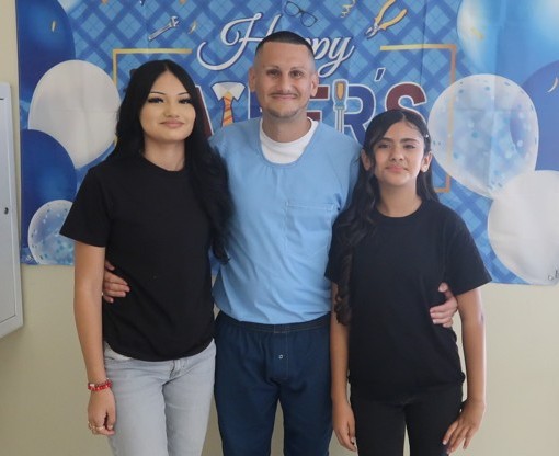Two people and an incarcerated person in front of a Father's Day photo backdrop at Avenal State Prison.