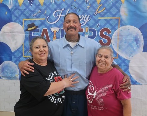 Two women and an incarcerated person take a photo during Father's Day visiting at Avenal State Prison.
