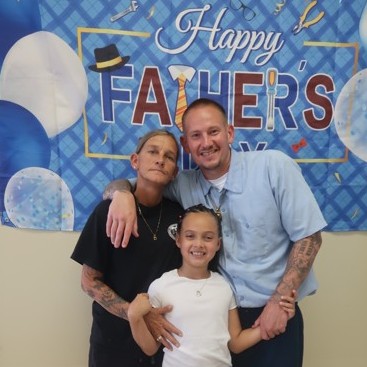 A woman, child and incarcerated person pose for a photo during Father's Day visiting at Avenal State Prison.