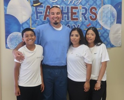 An incarcerated person with three visitors posing for a photo during Father's Day visiting at Avenal State Prison.