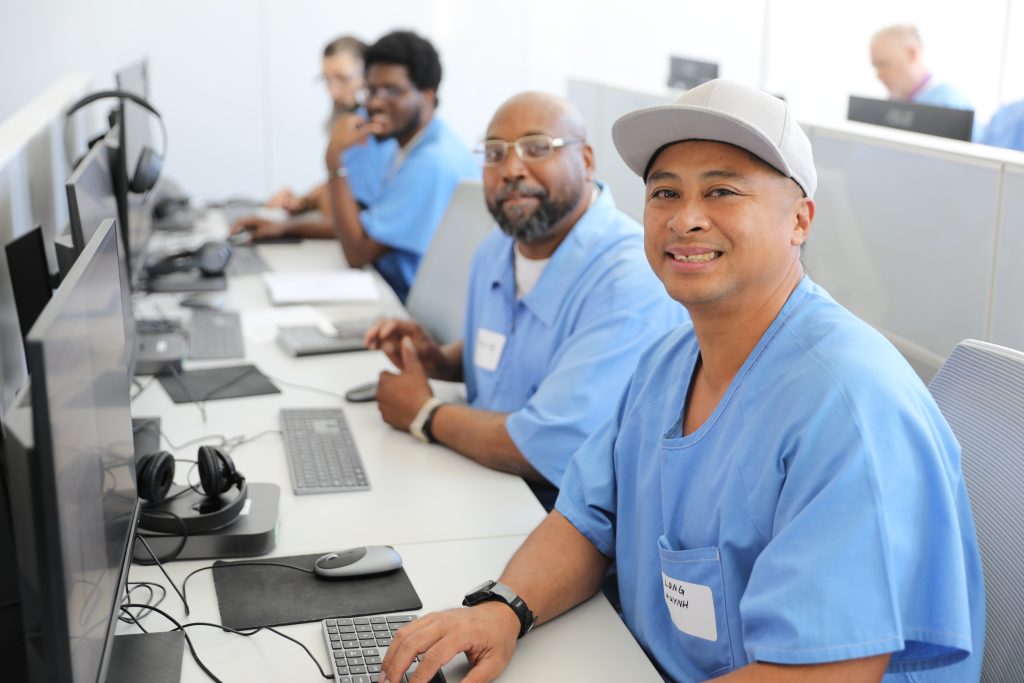 Incarcerated men sitting at computer terminals demonstrating coding skills they've learned to help them land jobs when they are released from serving their sentences with the California Department of Corrections and Rehabilitation, or CDCR. They are shown as part of The Last Mile coding program offered at San Quentin Rehabilitation Center during a showcase for community partners and employers.
