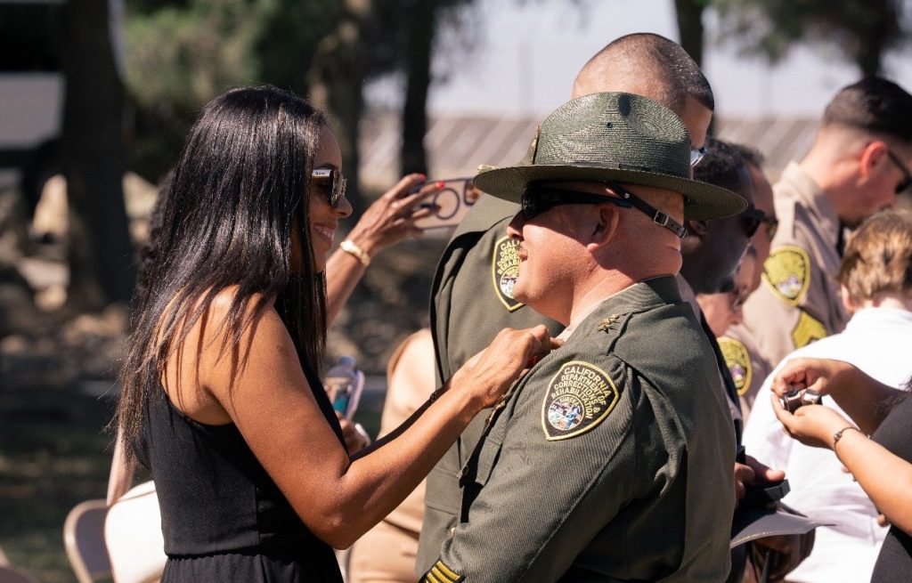 A family member pins new rank insignia on a staff member at CCWF during the fourth promotional ceremony.