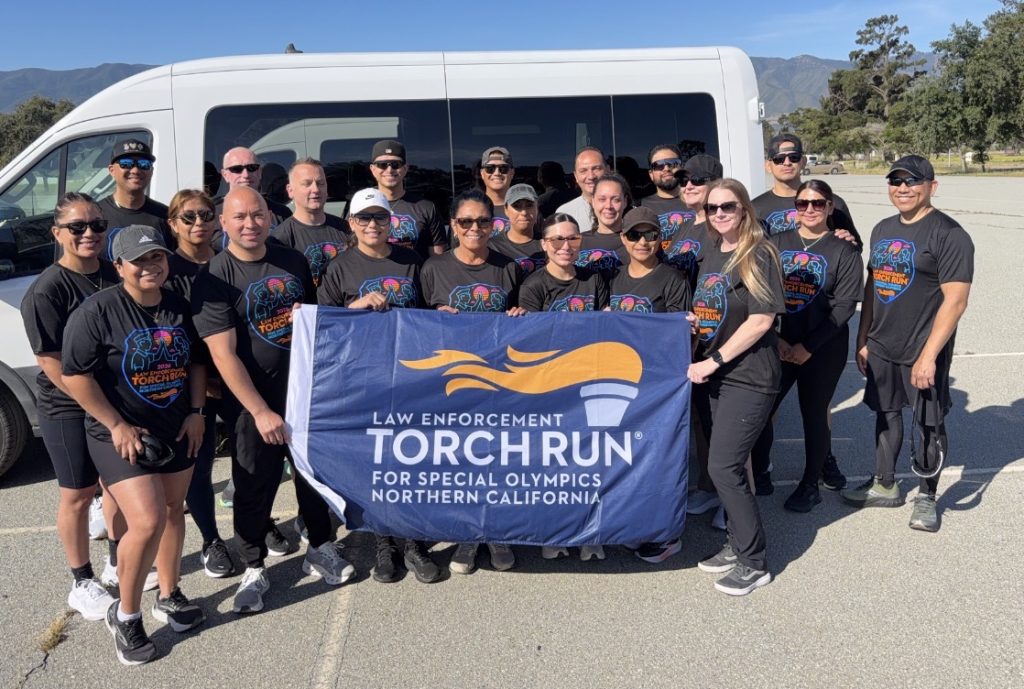 Group hold the Law Enforcement Torch Run flag while standing beside a van.