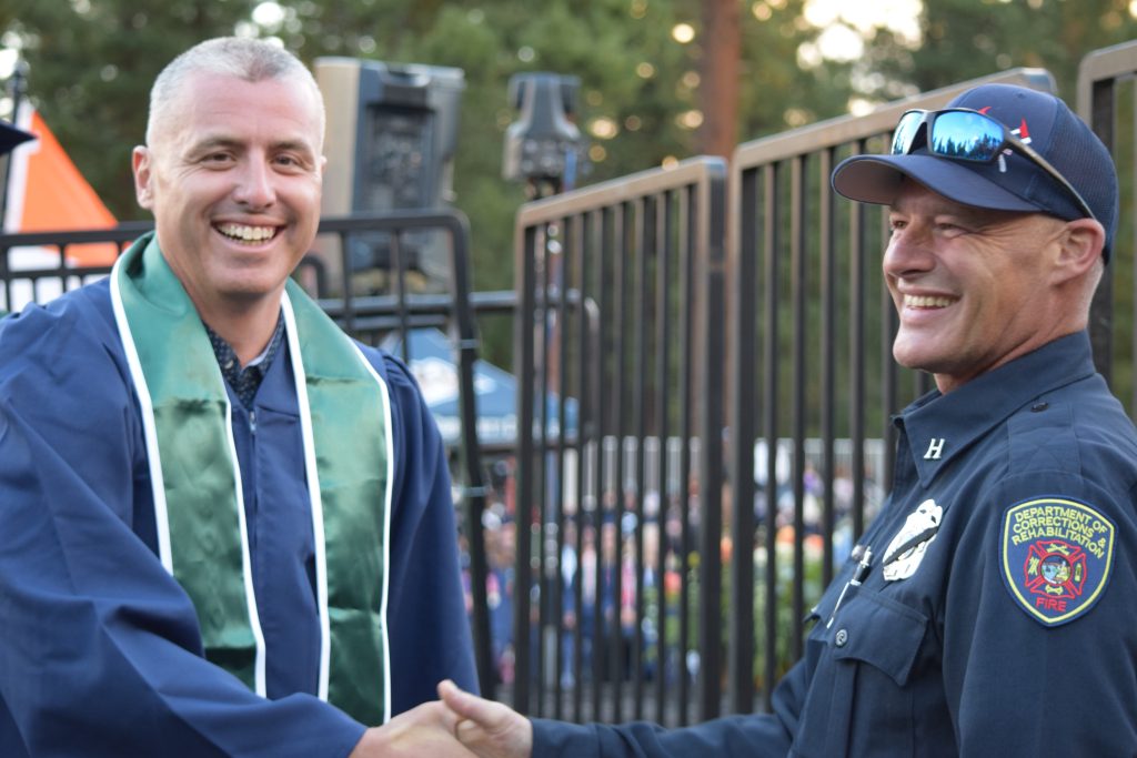 CDCR Fire staff member shakes hands with an incarcerated graduate.