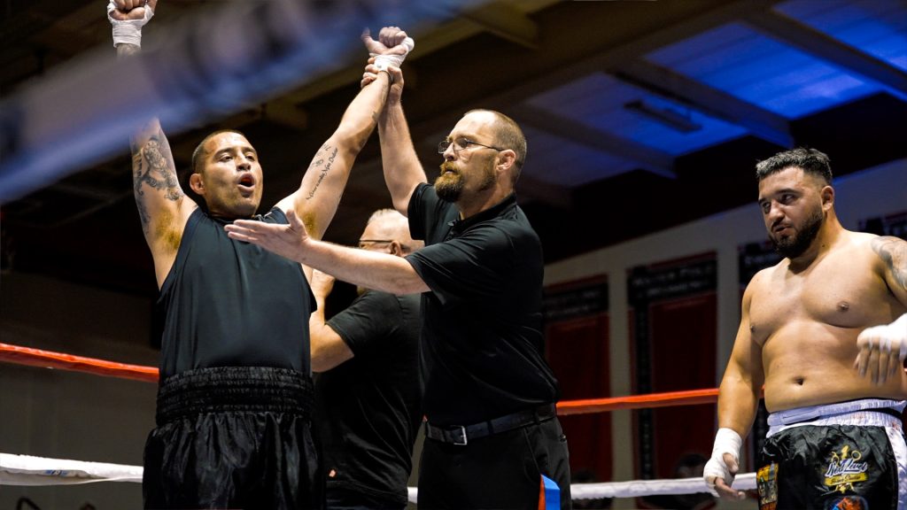 A correctional officer in the boxing ring with the referee holding up his hand in victory.