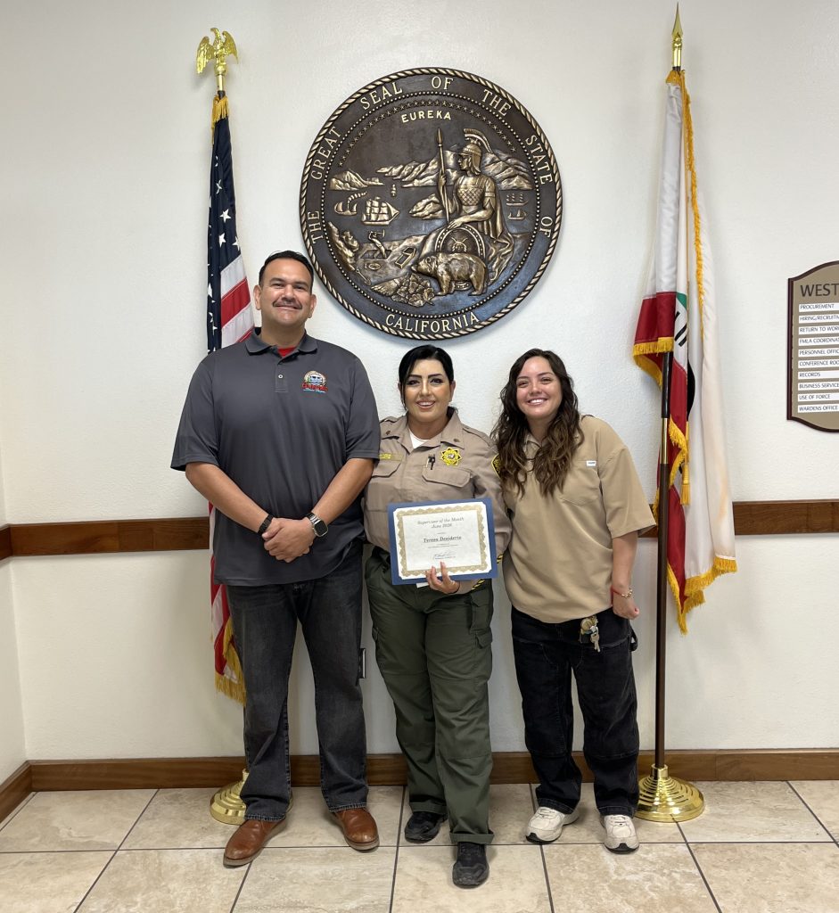 A custody staff member holds a certificate at Calipatria State Prison, flanked with two other people.